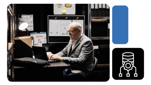 Homem maduro de terno trabalha em notebook em sala de arquivos com gráficos de dados na parede; ícone remete a banco de dados automatizado.